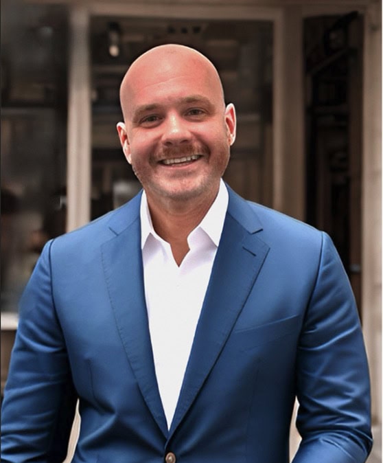 Man wearing suit and tie standing outside building with white shirt.